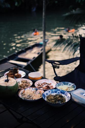 a table with plates of food on a table near the water at Decoco Canal-side Homestay in Ban Khlong Duang