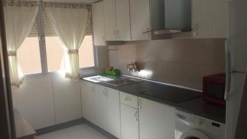 a kitchen with white cabinets and a window and a sink at Tres Cruces Apartment in Las Navas del Marqués