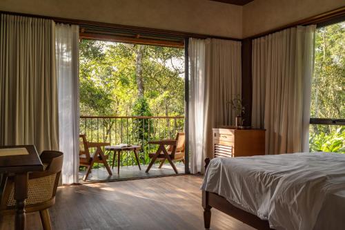 a bedroom with a bed and a balcony with a table and chairs at CardMem Hills View Pool Villa & Resort, Thekkady in Thekkady