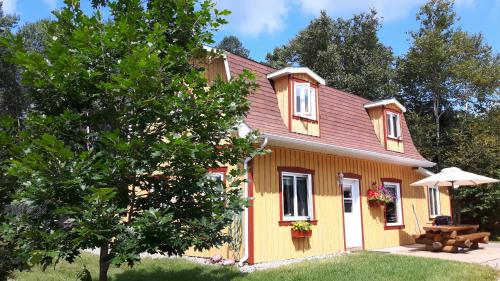 une maison jaune avec une table et un parasol dans l'établissement Grangette Entre Chiens et Loups, à LʼAnse-Saint-Jean