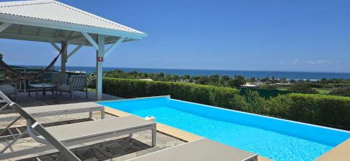 a blue swimming pool with a table and a umbrella at Les villas "Fenêtres Sur Plage" - Villas Créoles de charme , vue exceptionnelle face mer et plage & piscines privées indépendantes vue mer in Saint-François