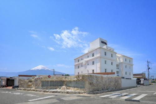 a white building with a mountain in the background at BE FREE HOTELS甲府は2025年8月にカップル専用のホテルをフルリノベーションした まったく新しいスタイルのホテルです様々なご利用者様の自由な過ごし方を提供するホテルとしてBE FREE HOTELsと名付けました in Showa