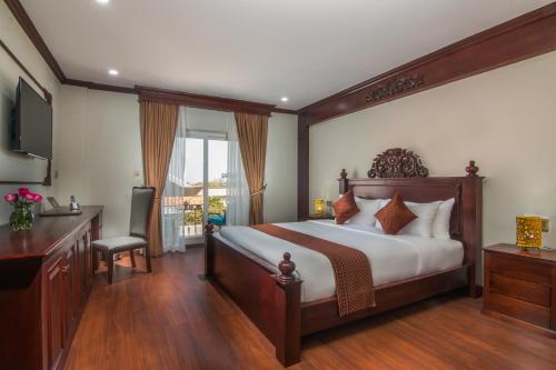 a bedroom with a bed and a desk and a television at Anachak Angkor Suite in Phumĭ Réach Born (1)