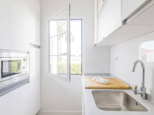 a white kitchen with a sink and a window at Siesta Mar Apartamentos in Cala en Porter