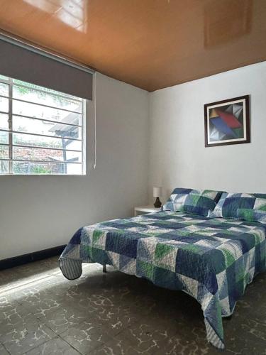 a bedroom with a bed with a plaid blanket and a window at The Cats Nail house in Cali