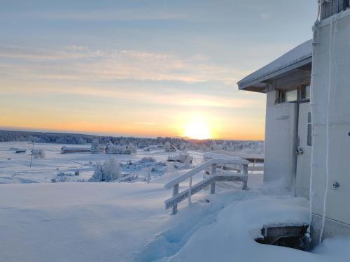 a winter sunset over a snowy field with a house at Lumikko Aurora Loft in Enontekiö