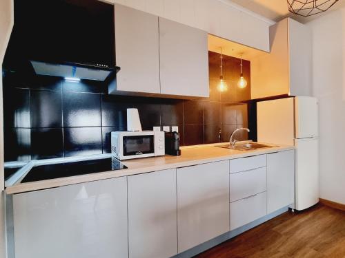 a kitchen with white cabinets and a microwave at Family Surf Home - Casas do Páteo in Ribamar