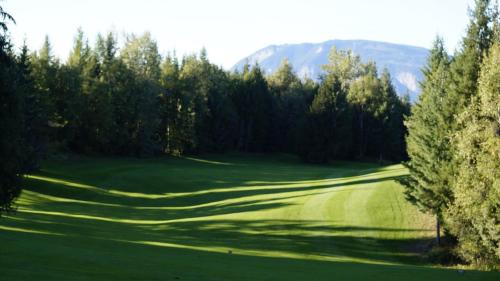a green golf course with trees and mountains in the background at The Inn at the Ninth Hole Bed & Breakfast in Salmon Arm
