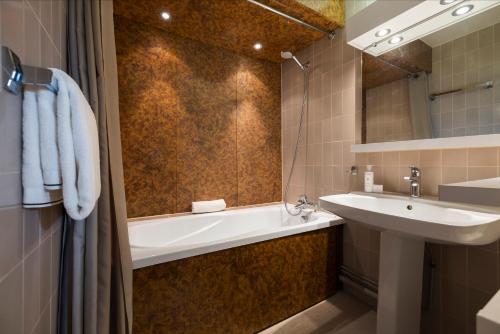 a bathroom with a sink and a bath tub and a mirror at Crystal Hôtel in Courchevel
