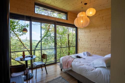 a bedroom with a bed and a table and windows at Les Coteaux - Lodges & Expériences in Laparade