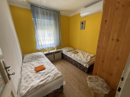 two beds in a room with yellow walls and a window at Anna Vendégház in Harkány