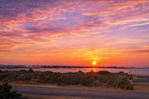 a sunset over a body of water with a road at Shell Town – Nags Head MP 16, Ocean View, 360 Yds to Beach, Pool, Hot Tub, Flex Stays in Nags Head