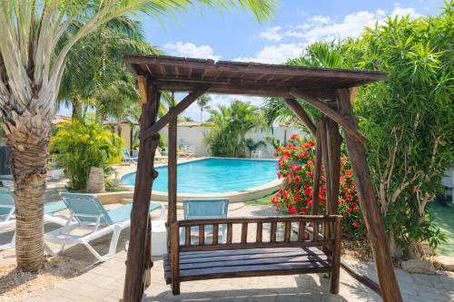 a wooden pergola with a bench next to a swimming pool at Casalina Garden 2 blocks to Palm Beach & Kitesurfing school in Palm-Eagle Beach