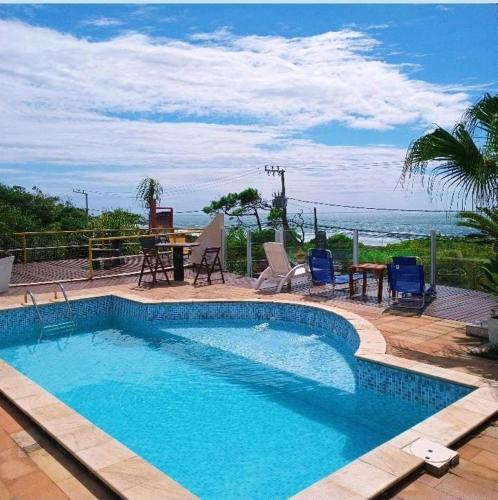 a swimming pool with a table and chairs and the ocean at Pousada Bangalôs Da Mole - Florianópolis in Florianópolis