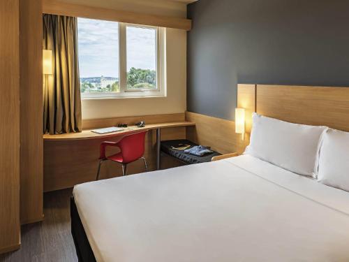 a hotel room with a bed and a desk and a window at ibis Chapeco in Chapecó