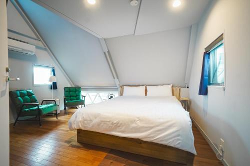 a bedroom with a white bed and green chairs at HennaWatei in Osaka