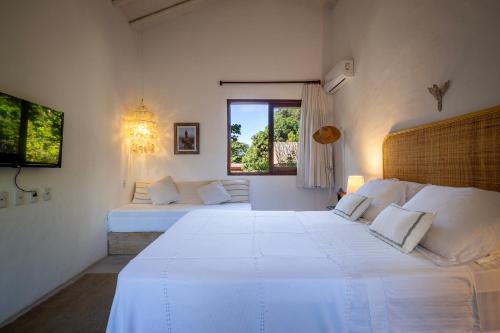 a white bedroom with two beds and a window at Casa Pini - Condomínio Altos de Trancoso, próxima ao Quadrado in Trancoso