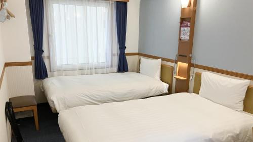 two beds in a small room with a window at Toyoko Inn Naha Omoromachi Ekimae in Naha