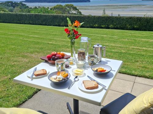a white table with breakfast foods and a vase of flowers at Mangawhai Bay B&B in Omokoroa