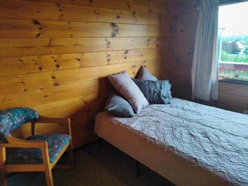 a bedroom with a wooden wall with a bed and a chair at Steve's Cozy Retreat in Taupo