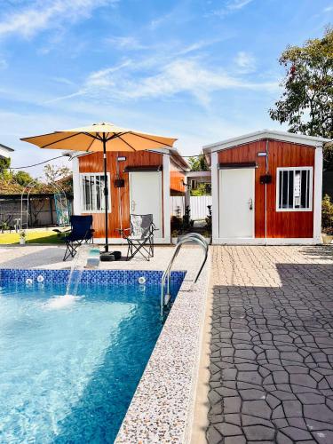 a swimming pool with an umbrella next to a building at Rossaliya Cottage in Taiping