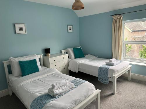 two beds in a room with blue walls and a window at Conwy Cottage in Conwy
