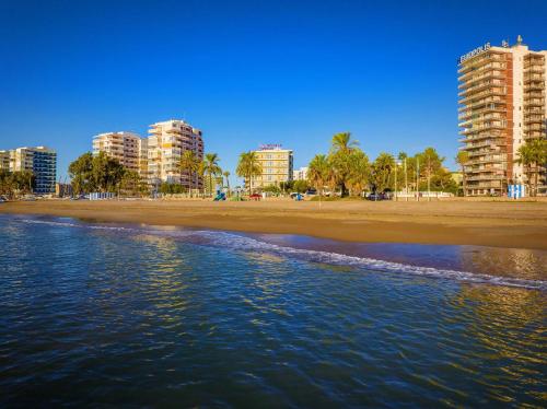 a beach with buildings and palm trees and the water at Hotel Servigroup Trinimar in Benicàssim
