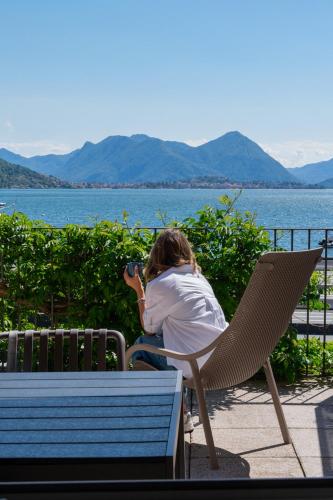 a person sitting on a bench taking a picture of the water at Regina e Oriente - La casa del Moro in Baveno