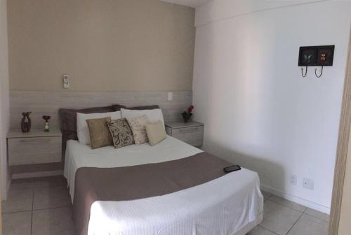 1 dormitorio con 1 cama con sábanas y almohadas blancas en Edifício Austrália JTR Maceió, en Maceió