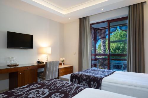 a hotel room with two beds and a desk and a window at Ali Bey Club & Park in Kizilagac