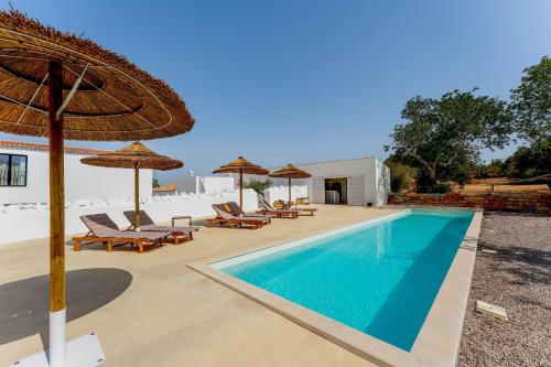 a pool with chairs and umbrellas next to a house at Uma Casa Rural in Santa Bárbara de Nexe