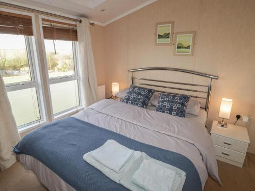 a bedroom with a bed with a blue blanket and two windows at Rhosgranog Caravan in Haverfordwest