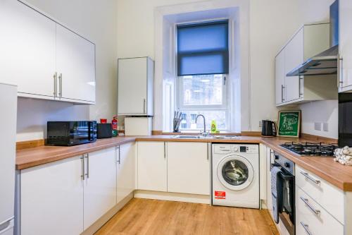 a kitchen with white cabinets and a washer and dryer at Cambridge Apartment in Glasgow