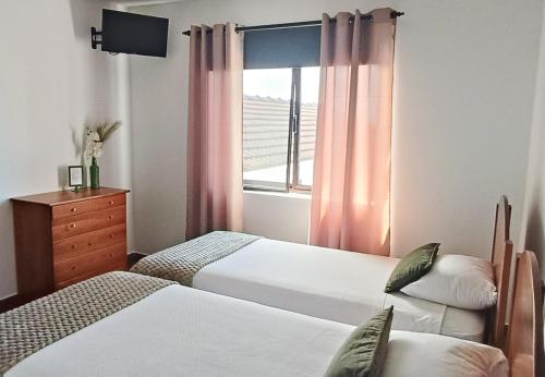a bedroom with two beds and a window with pink curtains at Faial Oceanfront Getaway AL in Horta
