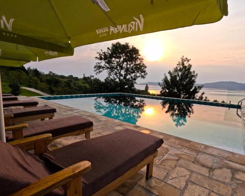 a pool with chairs and an umbrella and the sunset at Umutuzo Lodge Kivu Lake in Buhoro