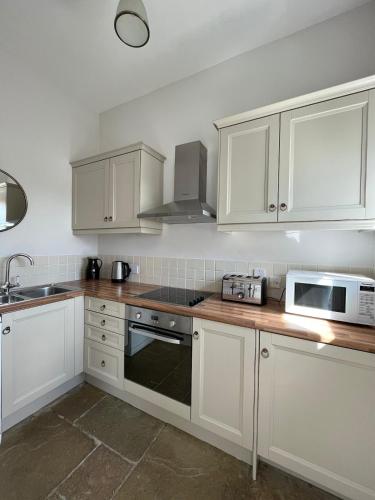 a kitchen with white cabinets and a sink and a microwave at The Stables in Corsley