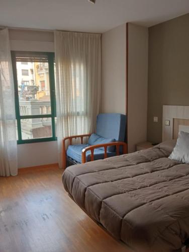 a bedroom with a bed and a chair and a window at Apartamentos xistra in Cangas del Narcea