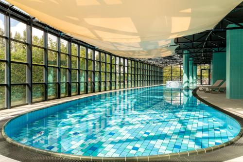 a large swimming pool with blue tiles in a building with windows at Corendon Urban Amsterdam Schiphol Airport Hotel in Badhoevedorp