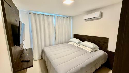 a bedroom with a bed with white sheets and a television at Chalé 02 centro de itapema in Itapema