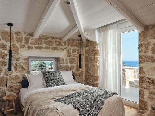 a bedroom with a stone wall with a bed and a window at Astarte Villas - Arismari Villas in Vasilikos