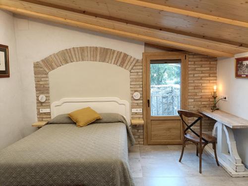 a bedroom with a bed and a desk and a window at El Freixe de l'Ylla in Els Hostalets