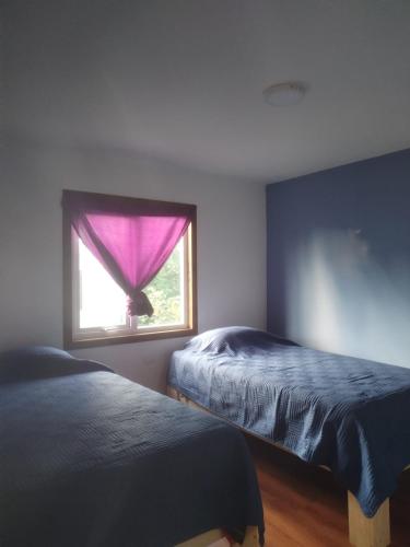 a bedroom with two beds and a window with a purple curtain at Cabañas Drü 3 in Coihaique
