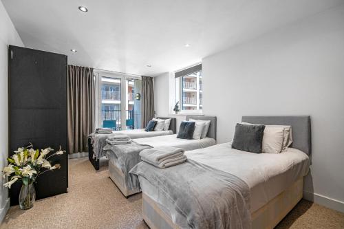 a room with three beds and a vase of flowers at Spacious Excel London Apartment with Balcony, River View and Parking Sleeps 8 in London