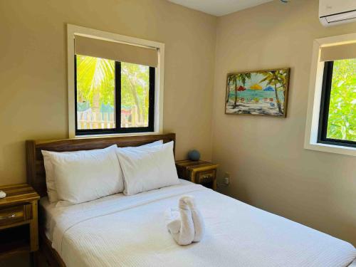 a bedroom with a white bed with two windows at The Flying Toucan Beach Rentals in Placencia