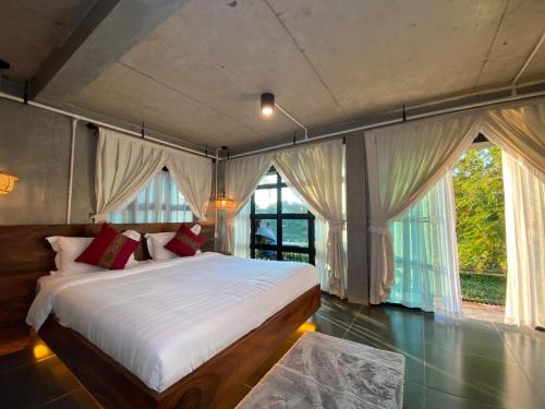 a bedroom with a large bed with curtains and windows at Namkhan Rivora Resort in Luang Prabang