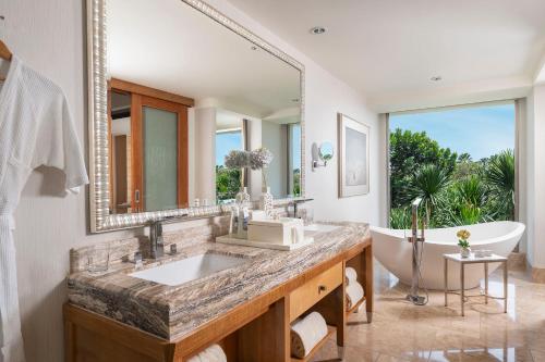 ein Badezimmer mit einem großen Spiegel, einer Badewanne und einem Waschbecken in der Unterkunft Mulia Resort in Nusa Dua