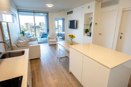 a kitchen with white cabinets and a living room at Modern City Pad, 1-Min to Showgrounds in Brisbane