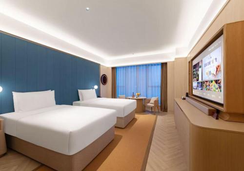 a hotel room with two beds and a flat screen tv at Orange Crystal Hotel Wuhan Jinyinhu in Dongxihu