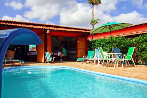 a swimming pool with chairs and a table and an umbrella at Pousada Curva do Sol in São Miguel do Gostoso