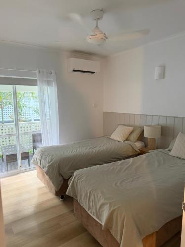 two beds in a white bedroom with a window at Tropical Palms Port Douglas in Port Douglas